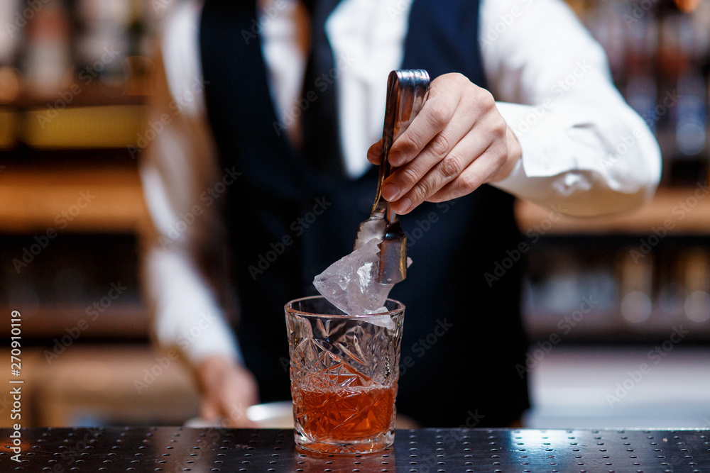 elegant young male bartender preparing a delicious cocktail at the bar. Bartender puts ice in a cocktail