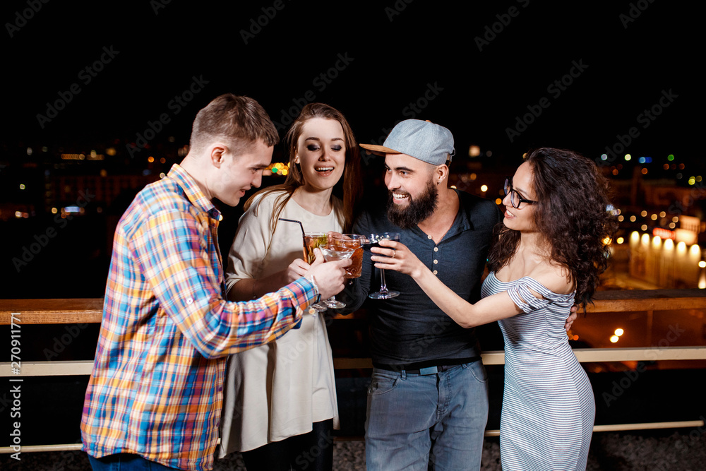 friends with smiles on their faces in the bar have fun, drink cocktails, clink glasses. friendly company celebrating on the roof against the backdrop of the night city friends with smiles on their faces in the bar have fun, drink cocktails, clink glasses. friendly company celebrating on the roof against the backdrop of the night city