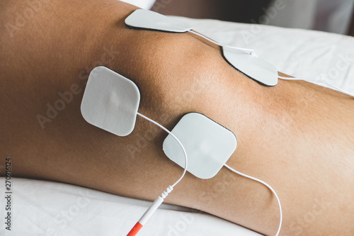 Patient applying electrical stimulation therapy on knee joint. Therapist placing electrodes on Knee. Electrical tens.