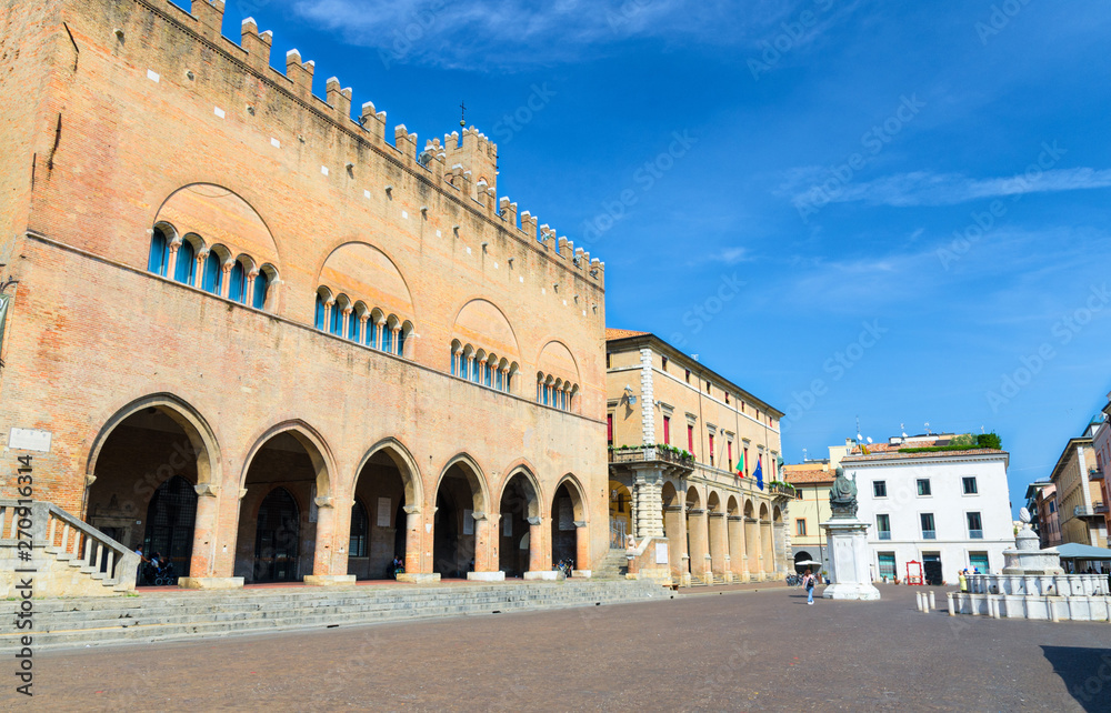 Palazzo dell'Arengo palace building with arches and Pope Paul V statue on Piazza Cavour square in old historical touristic city centre Rimini with blue sky background, Emilia-Romagna, Italy