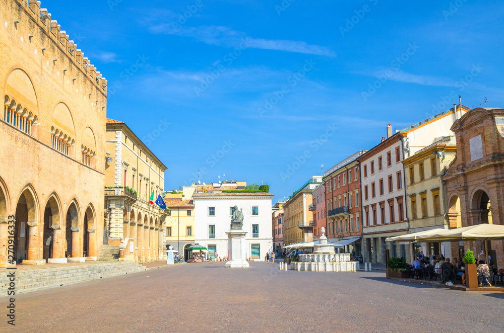 Old colorful multicolored building and houses and Pope Paul V monument on Piazza Cavour square in historical touristic city centre Rimini with blue sky background, Emilia-Romagna, Italy