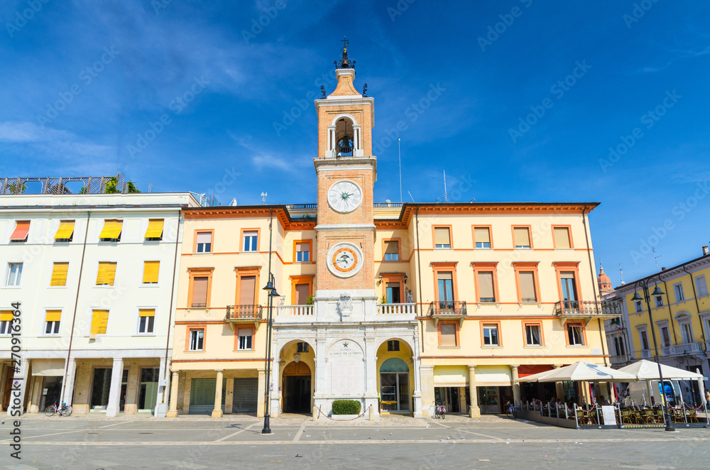 Traditional building with clock and bell tower on Piazza Tre Martiri Three Martyrs square in old historical touristic city centre Rimini with blue sky background, Emilia-Romagna, Italy