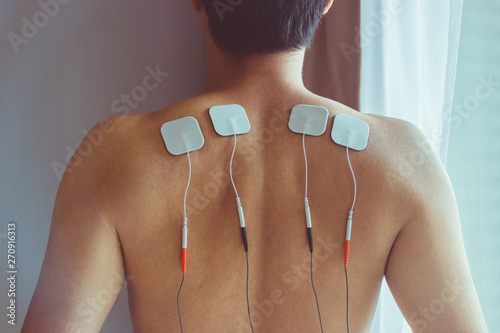 TENS treatment in physical therapy. Young man with TENS on his back and shoulders. photo