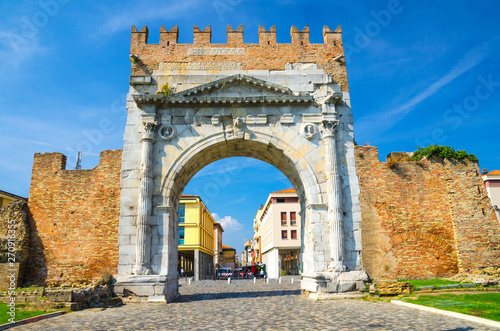 Ruins of ancient brick wall and stone gate Arch of Augustus Arco di Augusto and cobblestone road in old historical touristic city centre Rimini with blue sky background, Emilia-Romagna, Italy