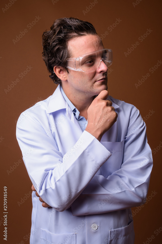 Italian man doctor wearing protective glasses against brown back Italian man doctor wearing protective glasses against brown back