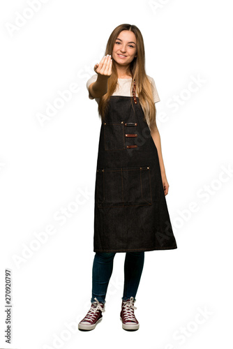 Full body Young woman with apron inviting to come with hand. Happy that you came on isolated background © luismolinero