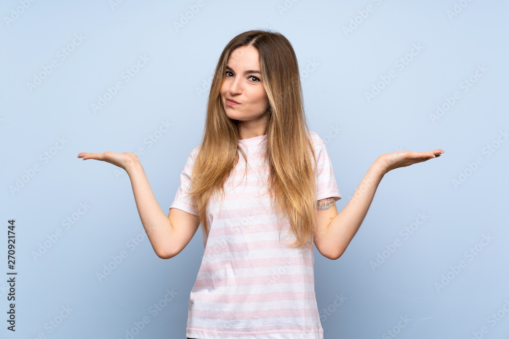 Young woman over isolated blue background having doubts while raising hands Young woman over isolated blue background having doubts while raising hands