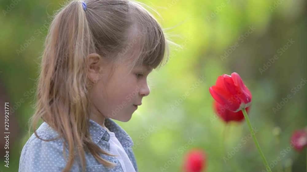 Young pretty child girl playing with a red tulip flower in summer outdoors. Young pretty child girl playing with a red tulip flower in summer outdoors.