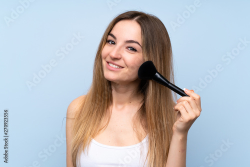 Young woman over isolated blue background with makeup brush