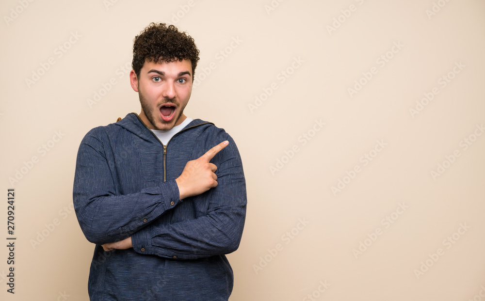 Man with curly hair over isolated wall surprised and pointing side Man with curly hair over isolated wall surprised and pointing side