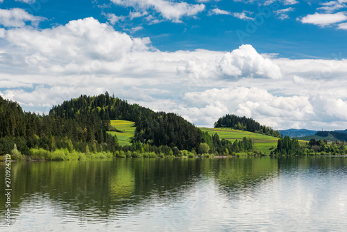 Serene landscape with green hills at lake, summer sunny day with clouds over blue sky