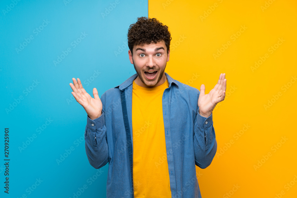 Man with curly hair over colorful wall with shocked facial expression Man with curly hair over colorful wall with shocked facial expression