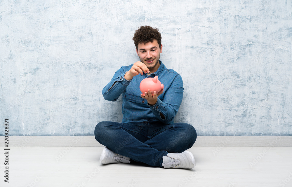 Young man sitting on the floor holding a big piggybank