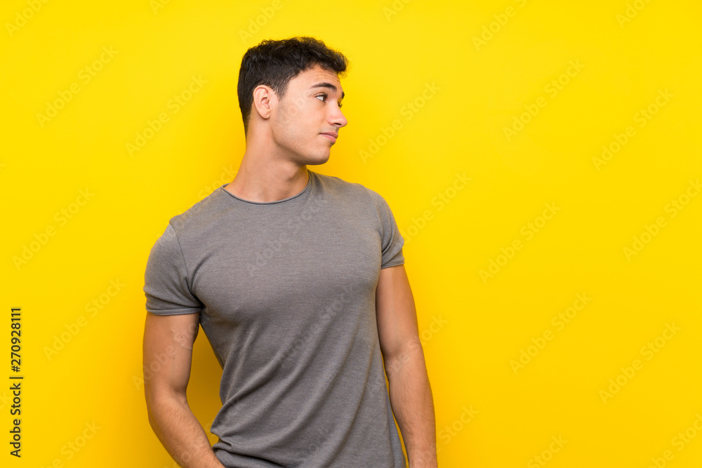 Obraz premium Handsome man over isolated yellow wall making doubts gesture looking side
