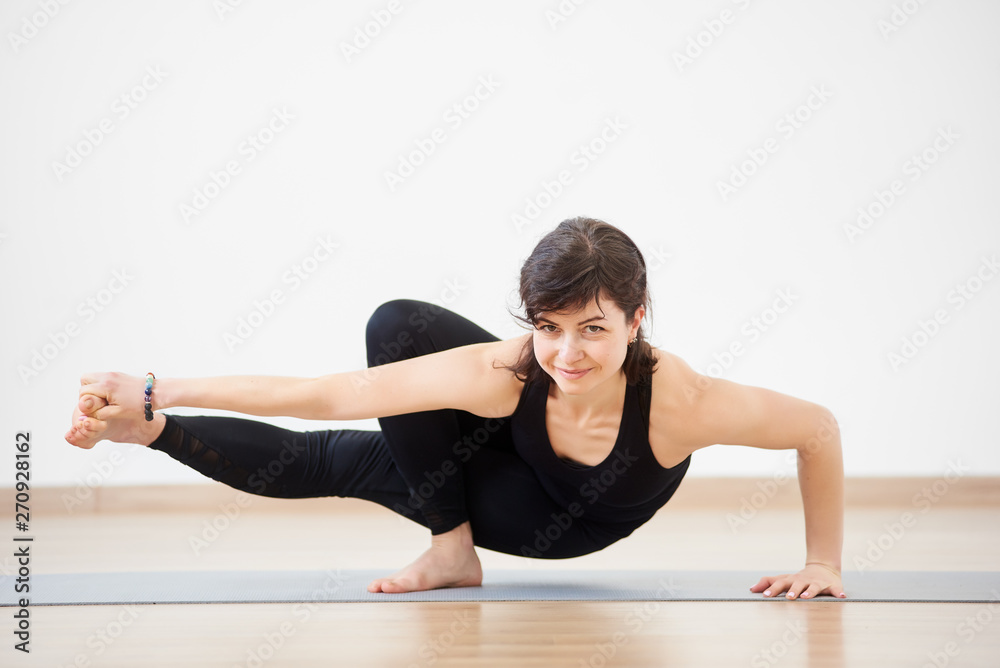 Athletic strong woman smiling practicing difficult yoga handstand pose,  balancing on one hand with one feet in air. Beautiful female yoga coach in  action. Yoga indoors concept. Copy space on top Stock