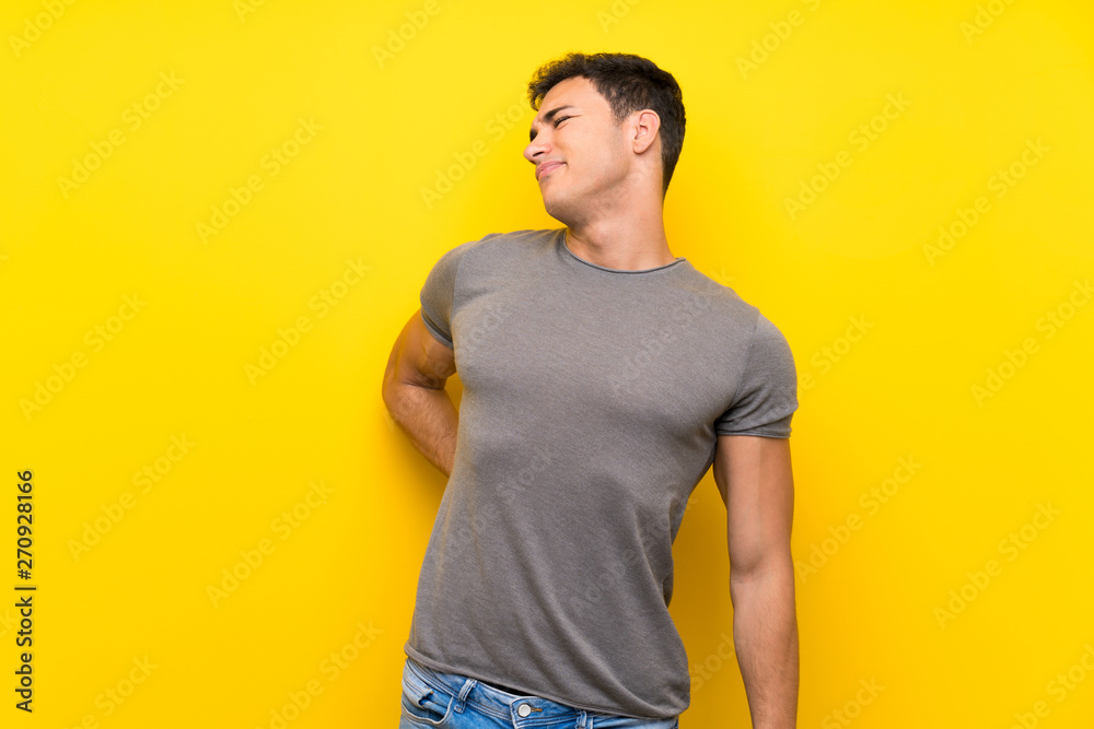 Handsome man over isolated yellow wall suffering from backache for having made an effort Handsome man over isolated yellow wall suffering from backache for having made an effort