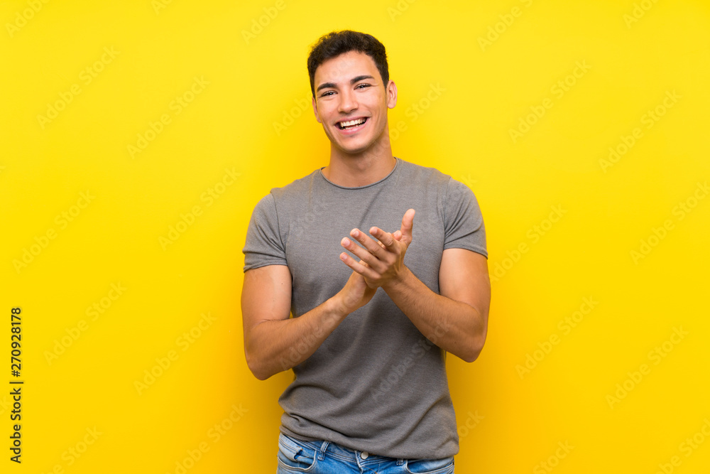 Handsome man over isolated yellow wall applauding after presentation in a conference