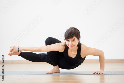 Athletic strong woman smiling practicing difficult yoga handstand pose,  balancing on one hand with one feet in air. Beautiful female yoga coach in  action. Yoga indoors concept. Copy space on top Stock Photo