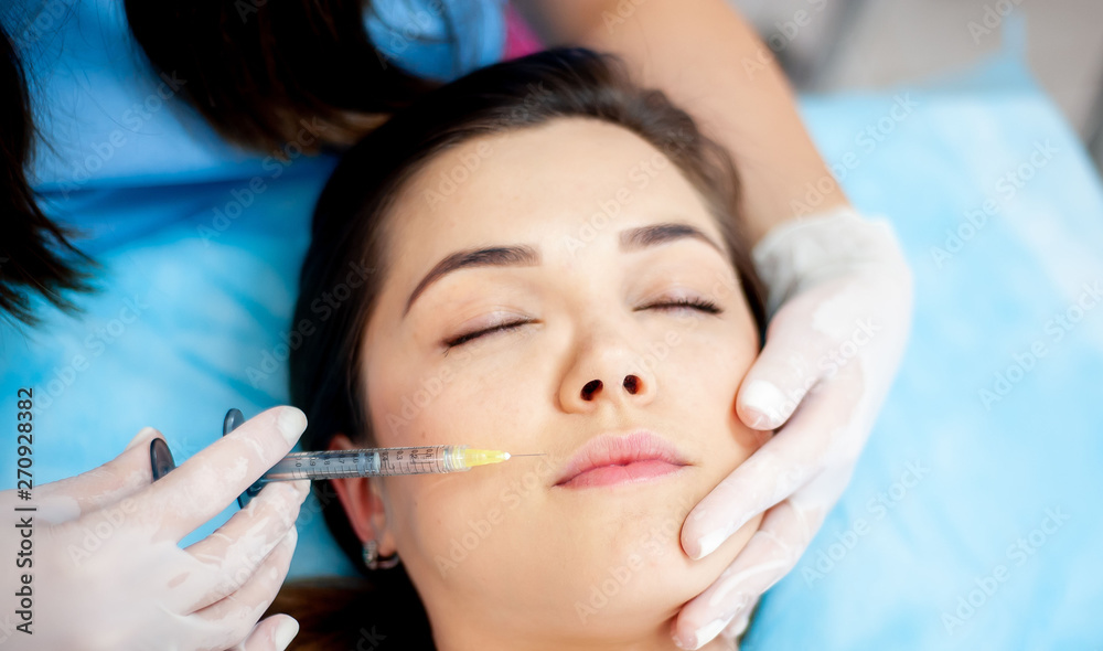Cosmetology clinic, cosmetologist doctor with a filler syringe for injection on the face. wrinkle treatment and facial contour correction. face plan