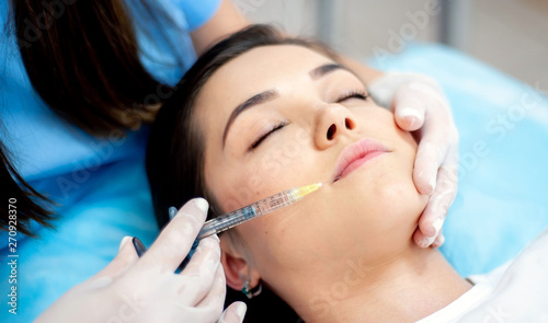 Cosmetology clinic  cosmetologist doctor with a filler syringe for injection on the face. wrinkle treatment and facial contour correction. face plan