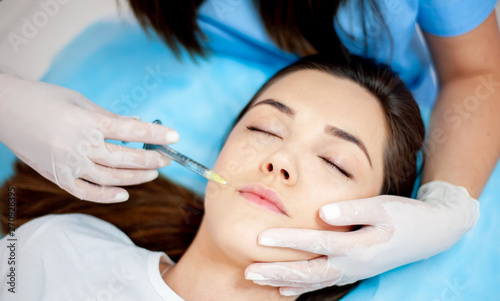 Cosmetology clinic, cosmetologist doctor with a filler syringe for injection on the face. wrinkle treatment and facial contour correction. face plan