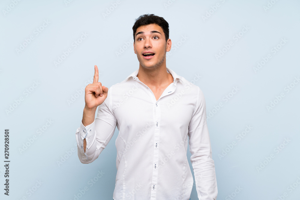 Handsome man over blue wall intending to realizes the solution while lifting a finger up Handsome man over blue wall intending to realizes the solution while lifting a finger up