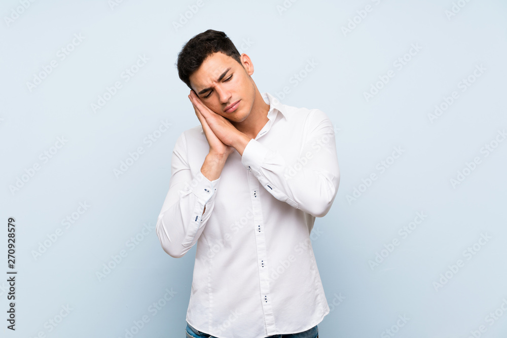 Handsome man over blue wall making sleep gesture in dorable expression Handsome man over blue wall making sleep gesture in dorable expression