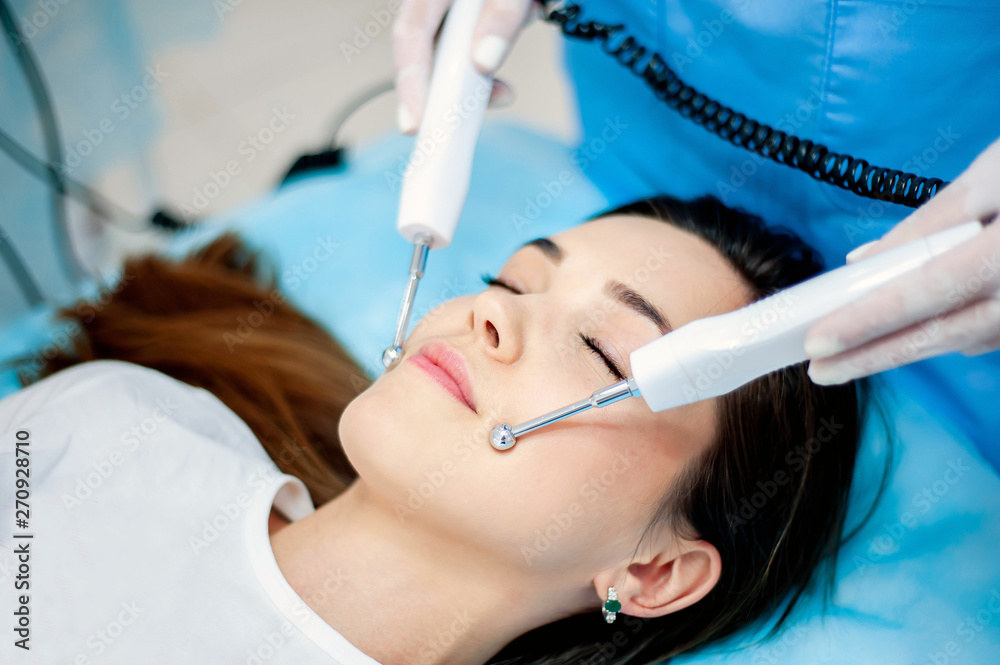 Fototapeta premium cosmetologist with a patient during facial procedures in a modern cosmetological and aesthetic clinic. A patient receives an electric facial massage. Skin rejuvenation and wrinkle smoothing.