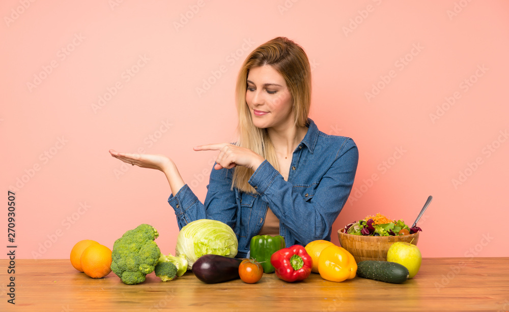 Young blonde woman with many vegetables holding copyspace imaginary on the palm to insert an ad Young blonde woman with many vegetables holding copyspace imaginary on the palm to insert an ad
