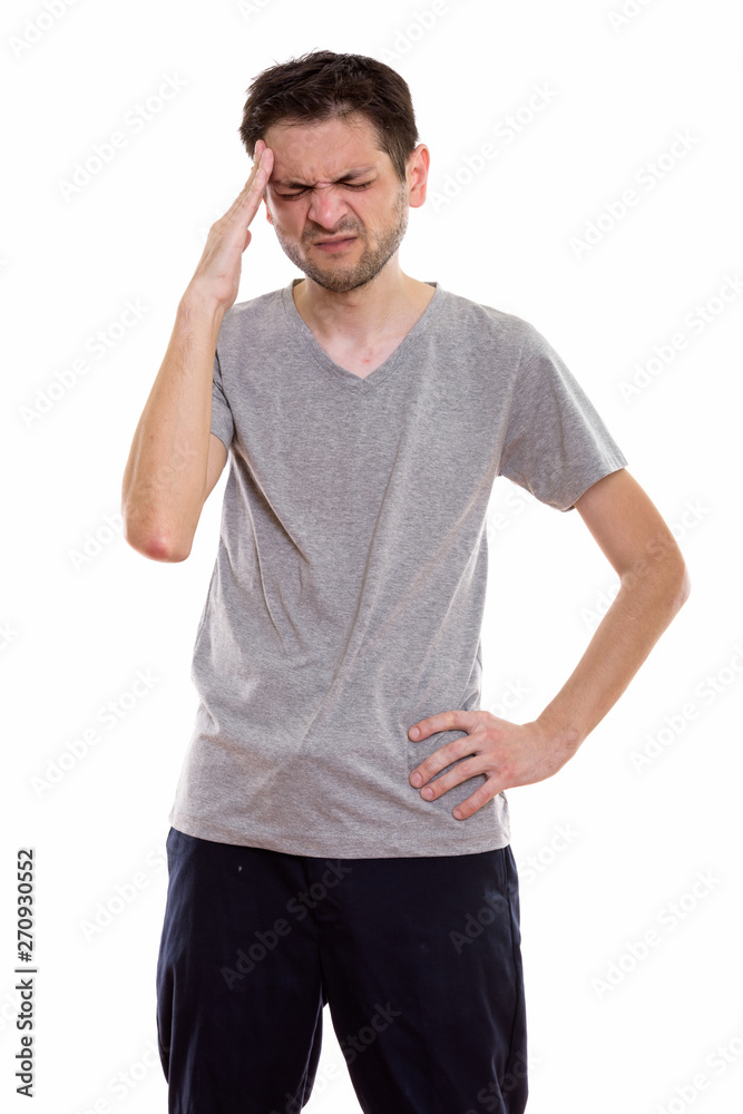 Studio shot of stressed young man standing while having headache Studio shot of stressed young man standing while having headache