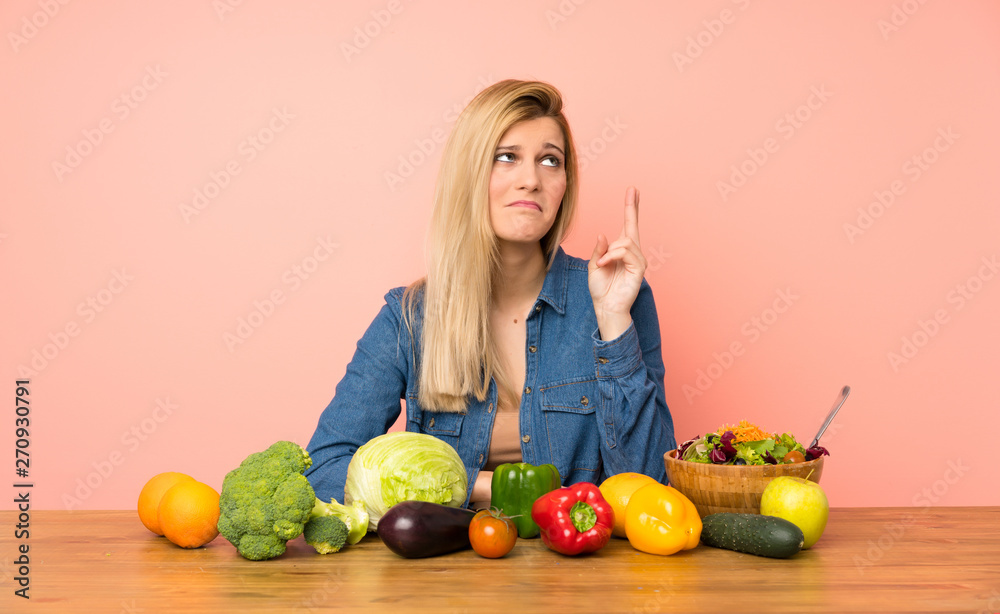 Young blonde woman with many vegetables with fingers crossing and wishing the best Young blonde woman with many vegetables with fingers crossing and wishing the best