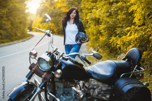attractive brunette motorcyclist standing near a motorcycle On the Sunset. adventure concept