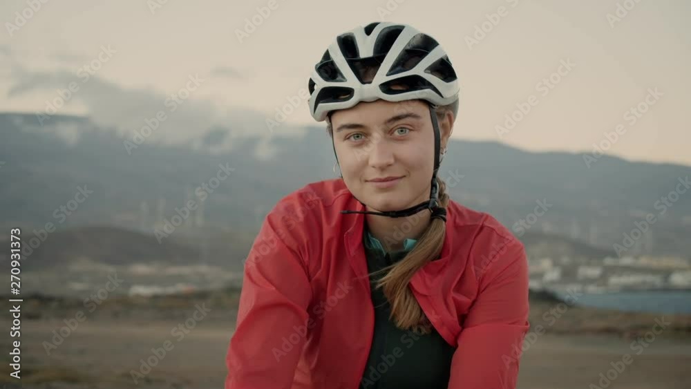 Beautiful athletic and sporty young woman in cycling gear, jersey, rain jacket and helmet, tired, exhausted but happy after hard training looks into camera with deep stare. Concept outdoor activity Beautiful athletic and sporty young woman in cycling gear, jersey, rain jacket and helmet, tired, exhausted but happy after hard training looks into camera with deep stare. Concept outdoor activity