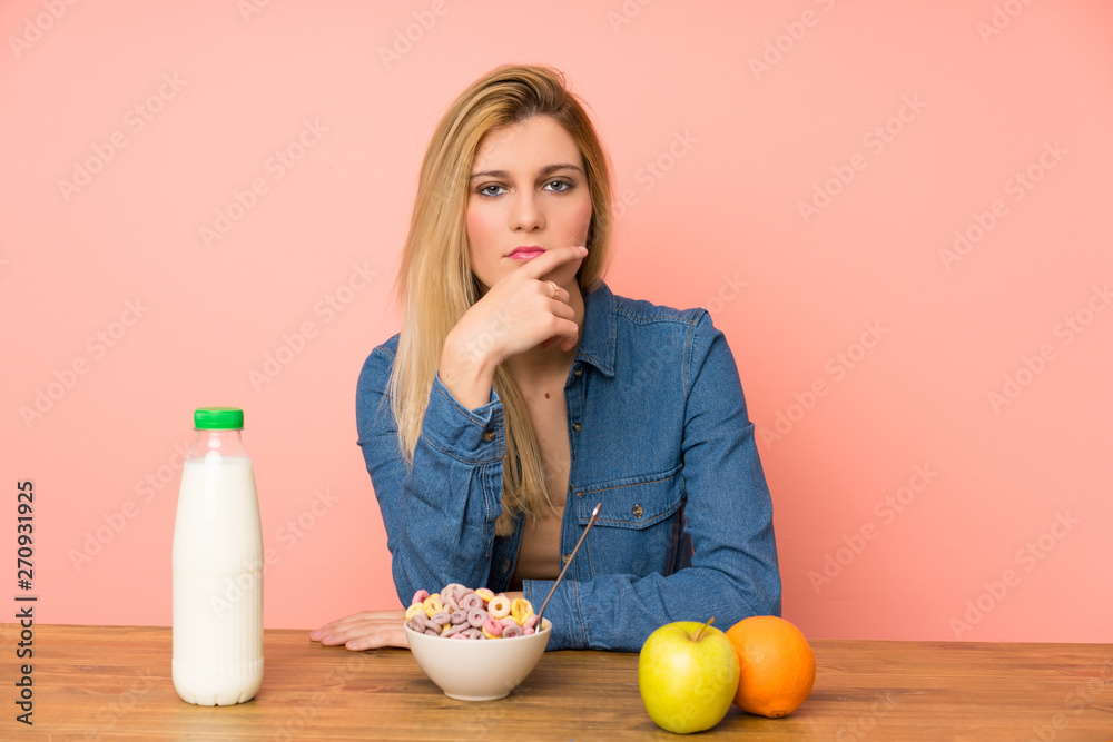 Young blonde woman with bowl of cereals standing and thinking an idea