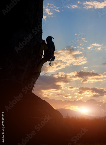 Side view of male silhouette climbing on natural rocky wall. Adrenaline, extreme, strength, ambition concept. Amazing mountain, sunrise with bright sunshine. Low angle view. Over filtered. Copy space