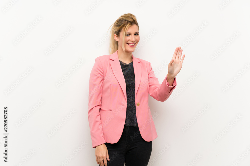Young blonde woman with pink suit saluting with hand with happy expression Young blonde woman with pink suit saluting with hand with happy expression