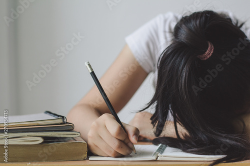 Tired teenager holding pencil and lying  sleeping on desk with book and homework. photo