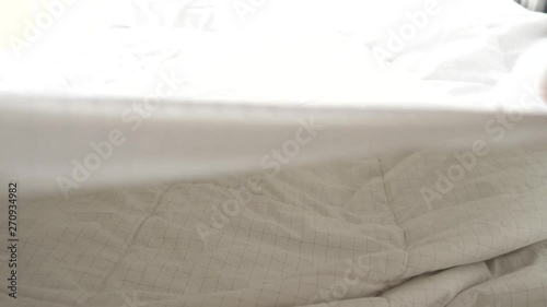 Hands bedding white blanket with natural light from window, slow motion
