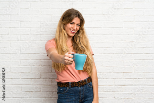 Young blonde woman over white brick wall holding hot cup of coffee © luismolinero