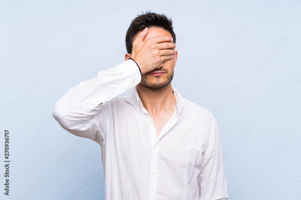 Handsome young man over isolated blue background covering eyes by hands. Do not want to see something Handsome young man over isolated blue background covering eyes by hands. Do not want to see something