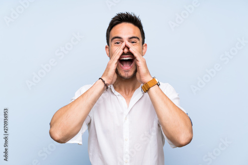 Handsome young man over isolated blue background shouting and announcing something