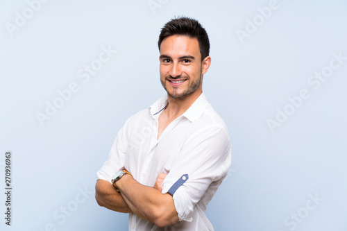 Handsome young man over isolated blue background with arms crossed and looking forward