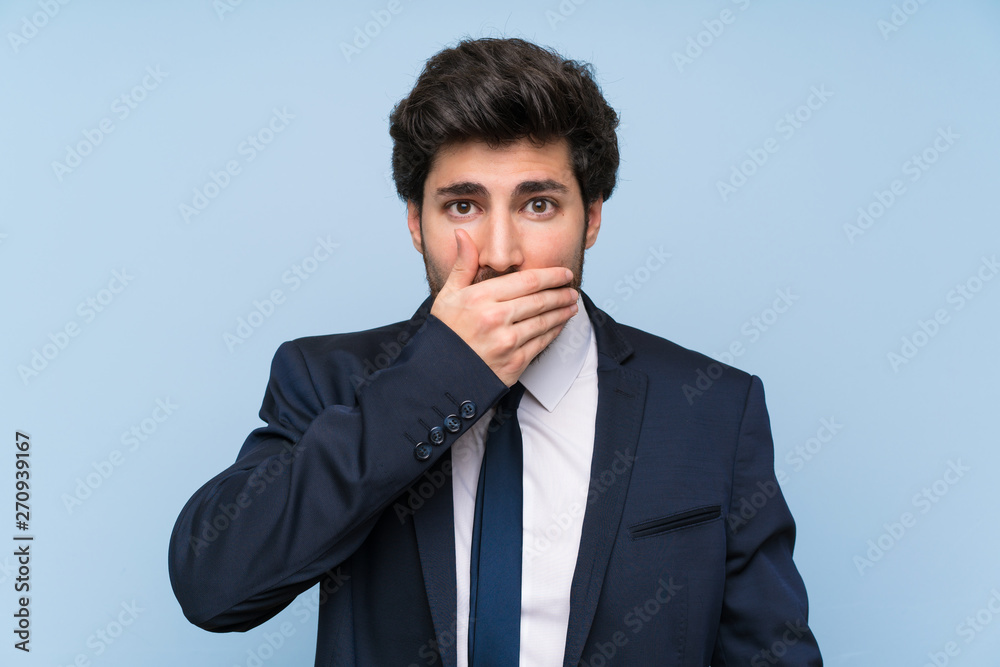 Businessman over isolated blue wall covering mouth with hands Businessman over isolated blue wall covering mouth with hands