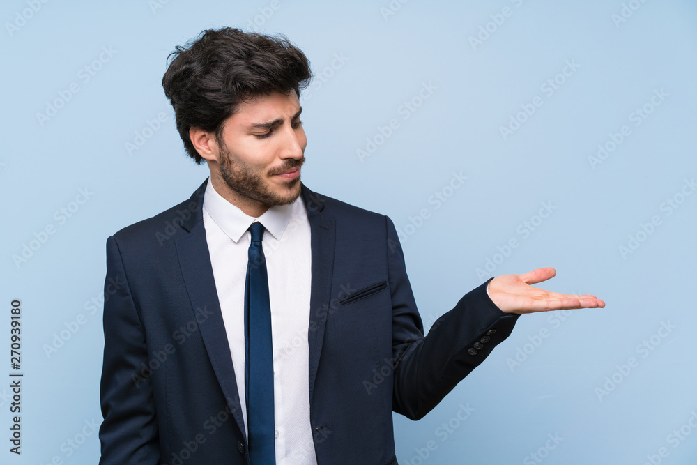 Businessman over isolated blue wall holding copyspace with doubts Businessman over isolated blue wall holding copyspace with doubts