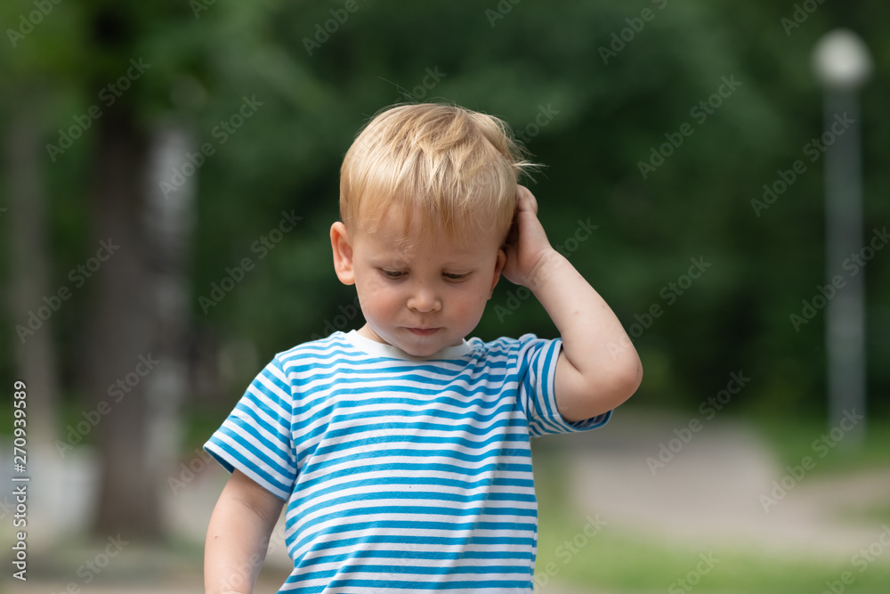 A little boy in a striped t-shirt scratching his head thoughtfully A little boy in a striped t-shirt scratching his head thoughtfully