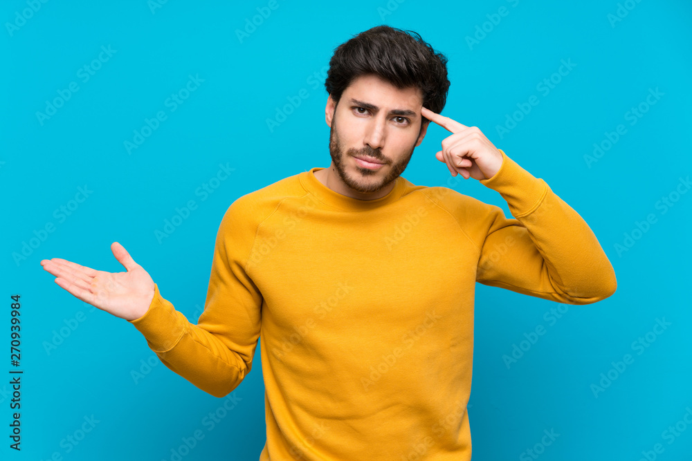 Handsome over isolated blue wall making the gesture of madness putting finger on the head Handsome over isolated blue wall making the gesture of madness putting finger on the head