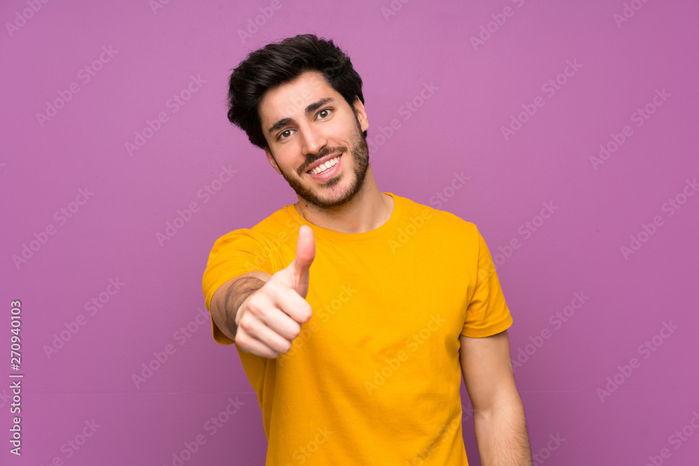 Handsome over isolated purple wall with thumbs up because something good has happened
