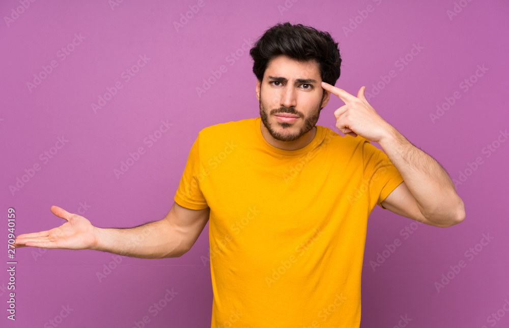 Handsome over isolated purple wall making the gesture of madness putting finger on the head Handsome over isolated purple wall making the gesture of madness putting finger on the head