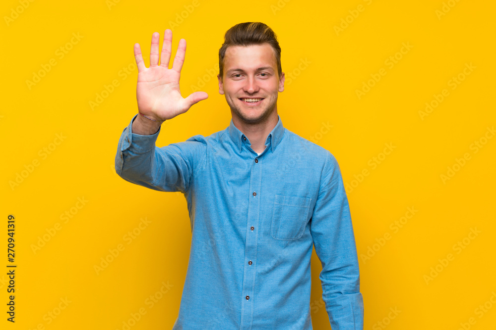 Blonde man over isolated yellow wall counting five with fingers Blonde man over isolated yellow wall counting five with fingers