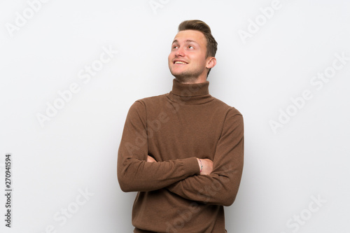 Blonde man over isolated white wall looking up while smiling